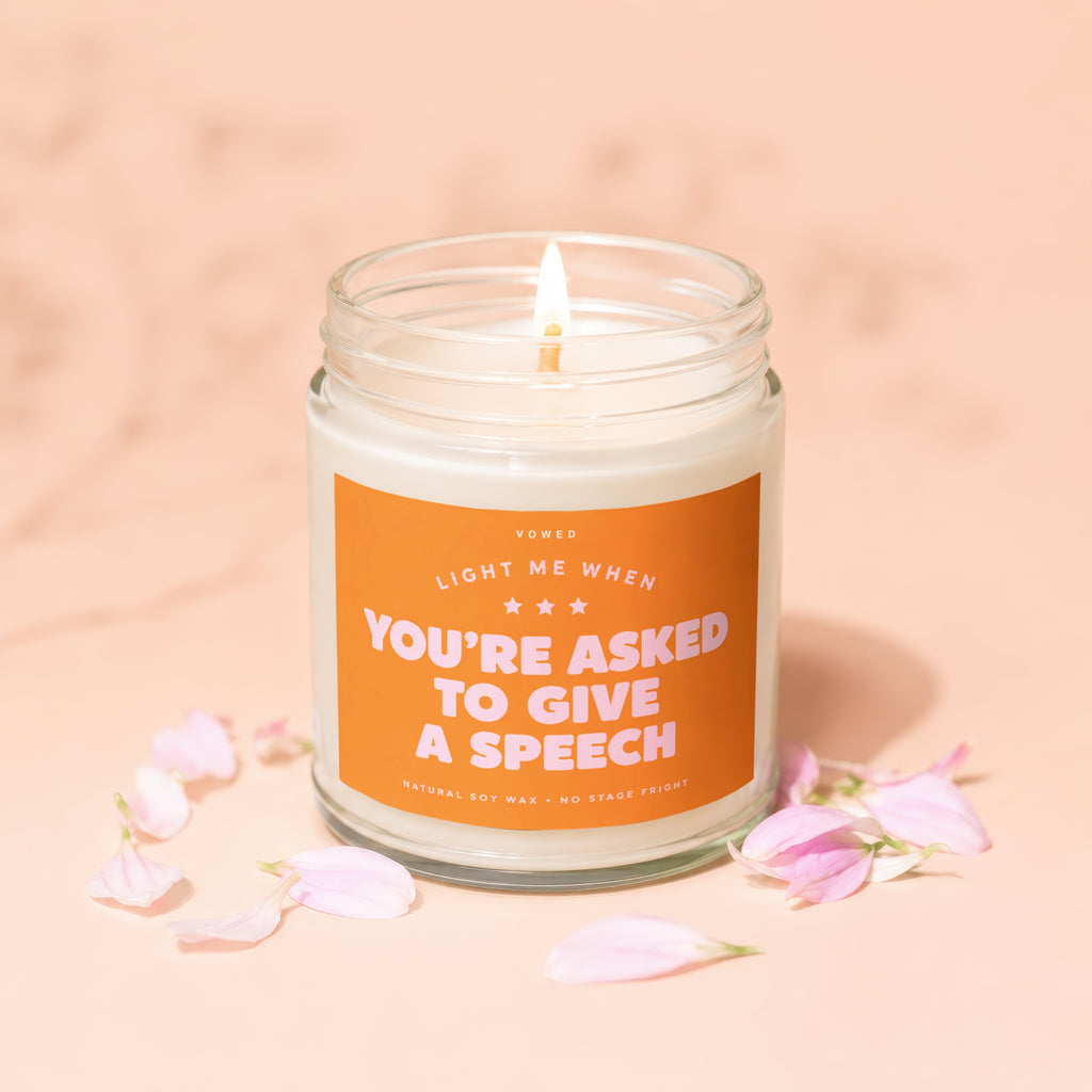 Scented candle with "You're Asked to Give a Speech" text, surrounded by pink petals.