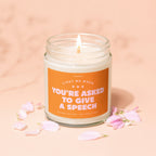 Scented candle with "You're Asked to Give a Speech" text, surrounded by pink petals.