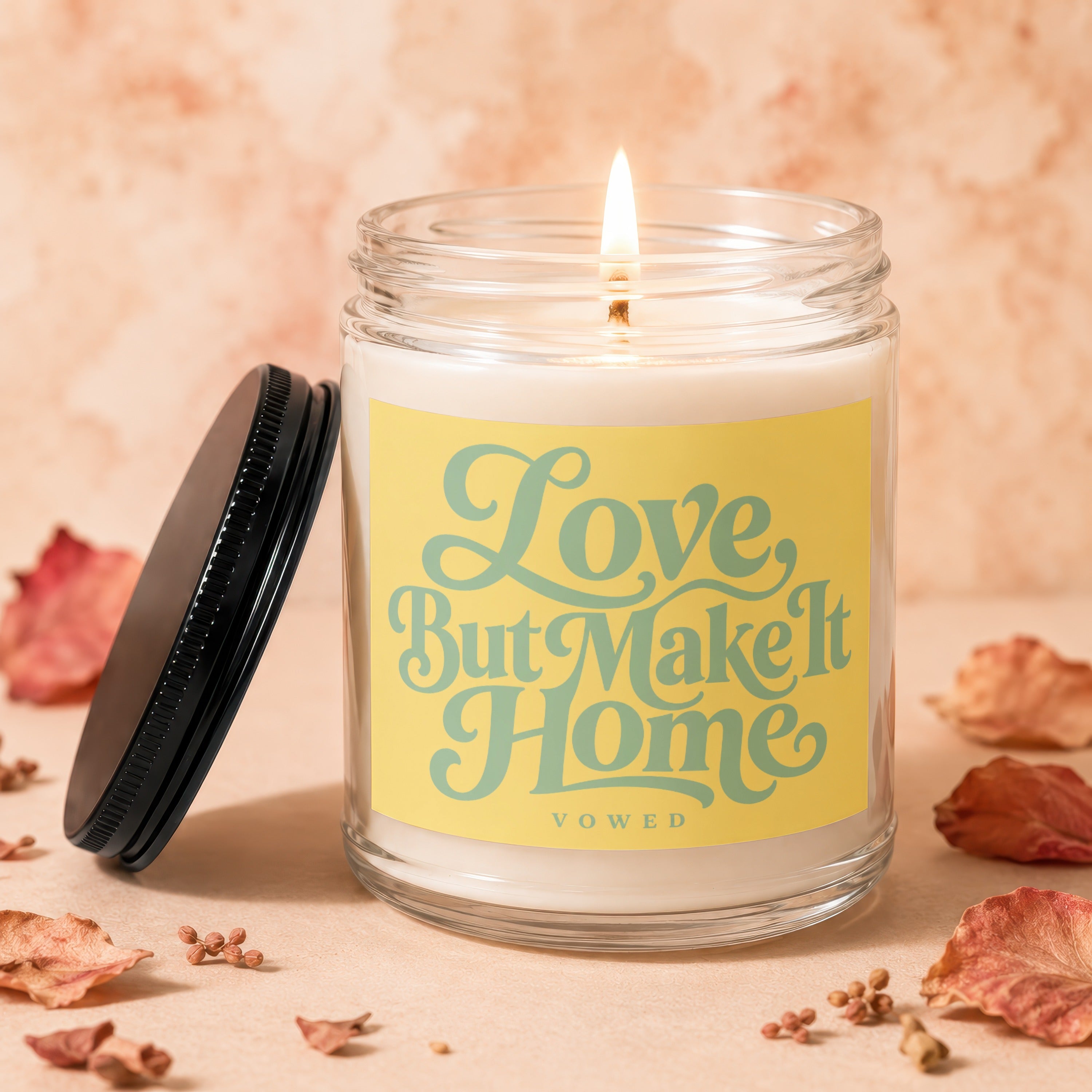 Jar candle with lit wick and yellow label reading "Love, But Make It Home Vowed".