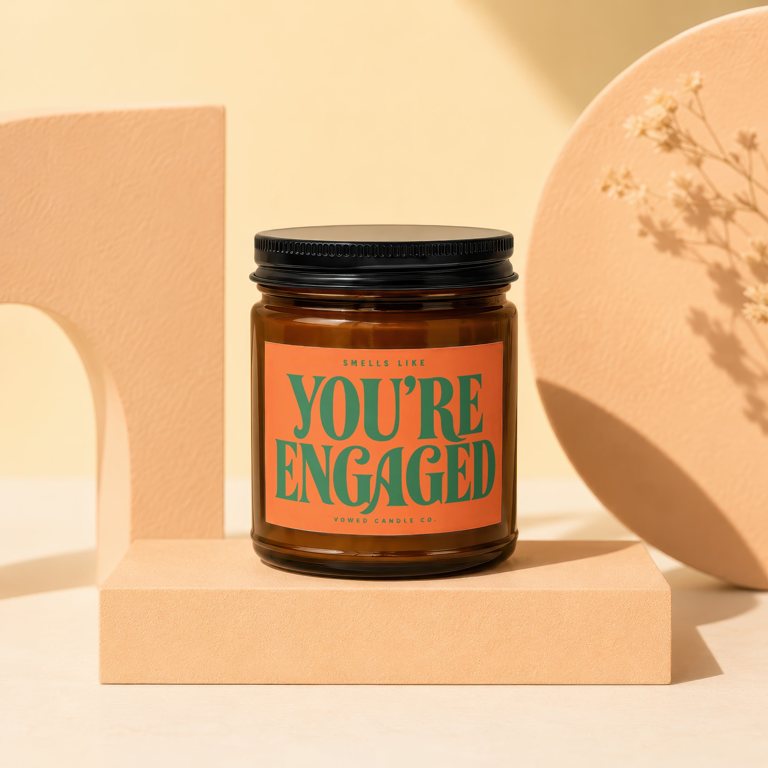 Amber candle with orange label reading "Smells Like You're Engaged" from Vowed Candle Co.