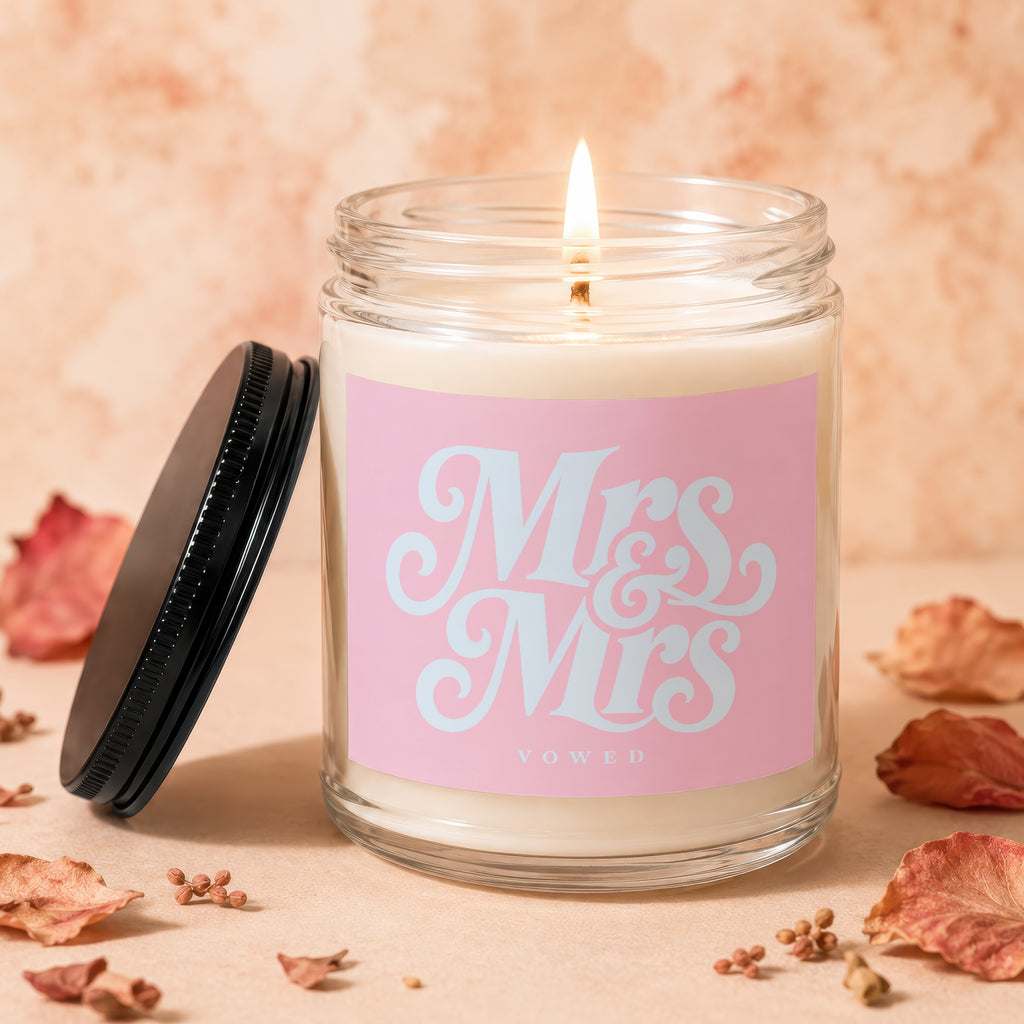 Jar candle with lit wick and pink label reading "Mrs & Mrs VOWED."