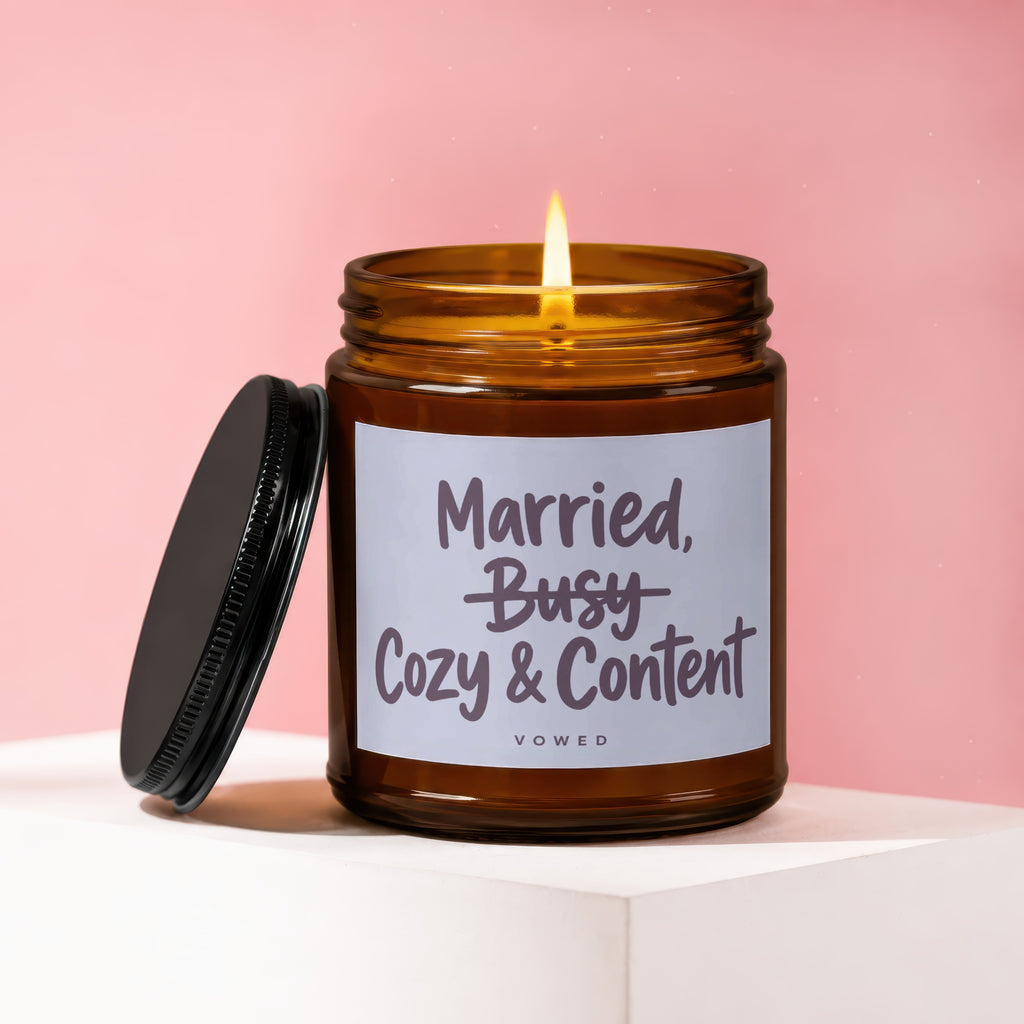 Amber candle with lit flame, lid off, reading "Married, Cozy & Content," VOWED.