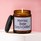 Amber candle with lit flame, lid off, reading "Married, Cozy & Content," VOWED.