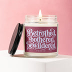 Glass jar candle with lit wick and maroon label reading "Betrothed, bothered, bewildered VOWED."