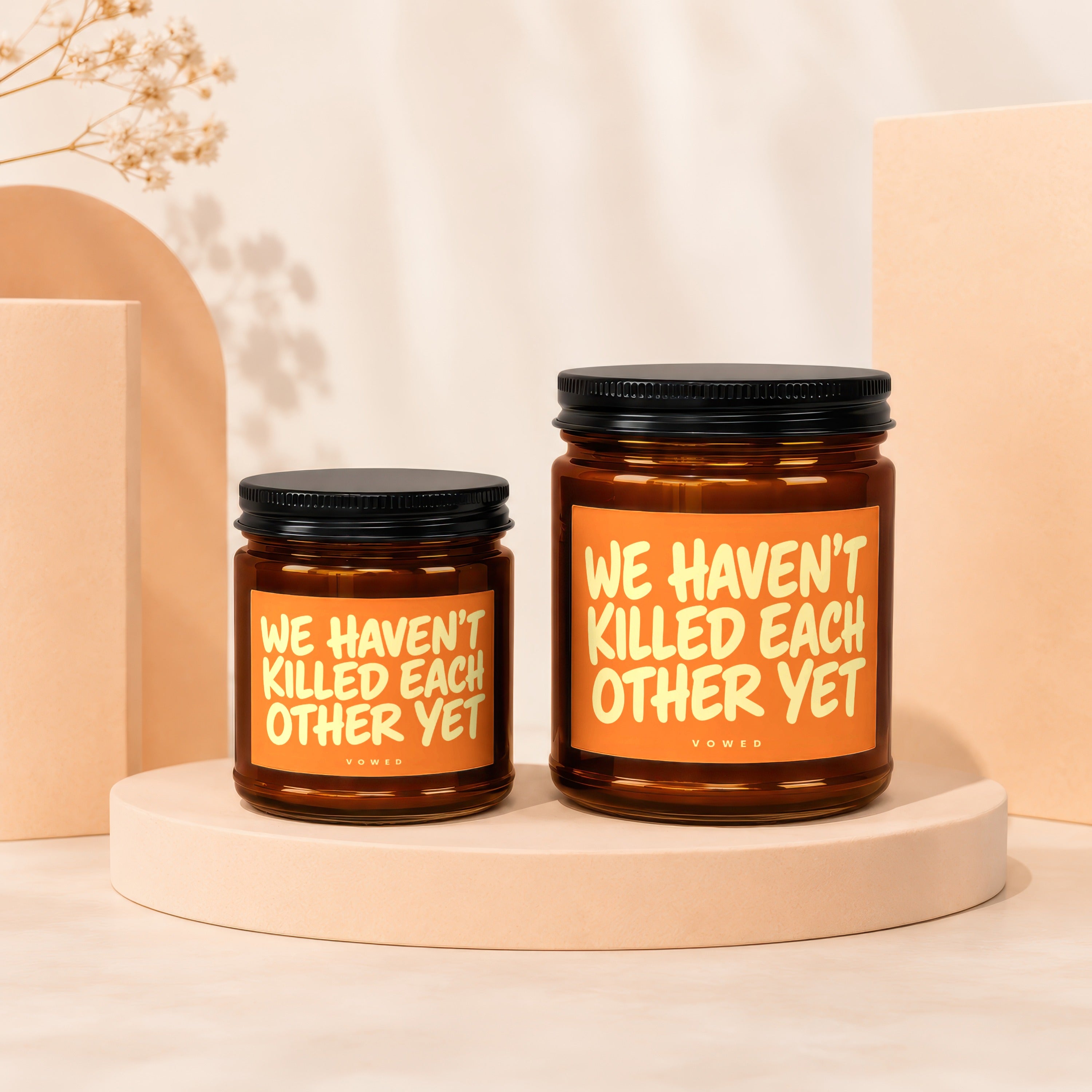Two amber glass candles with orange labels reading "WE HAVEN'T KILLED EACH OTHER YET".