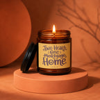 Amber jar candle with lit wick and label reading "Two Hearts, One Mortgage, Home".