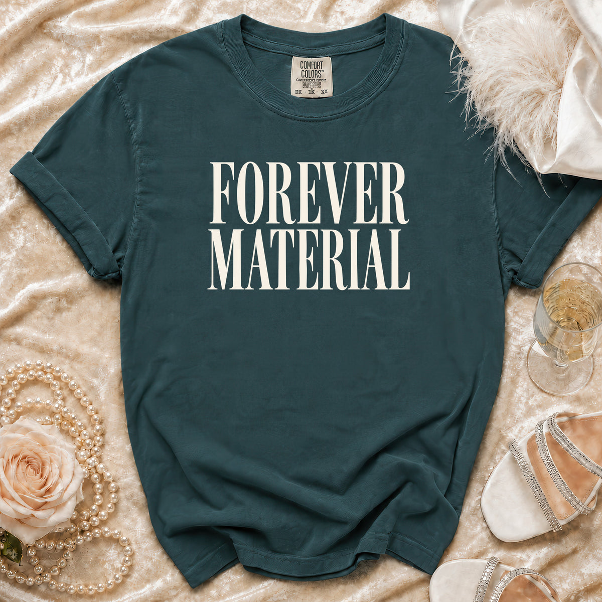 Teal t-shirt with "FOREVER MATERIAL" text, laid flat with accessories.
