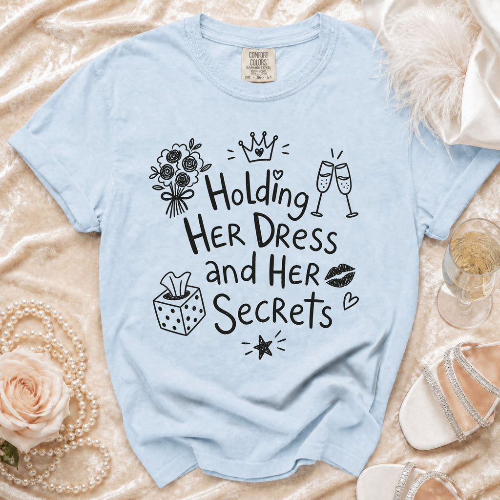 Light blue t-shirt with black graphic text "Holding Her Dress and Her Secrets", featuring icons.