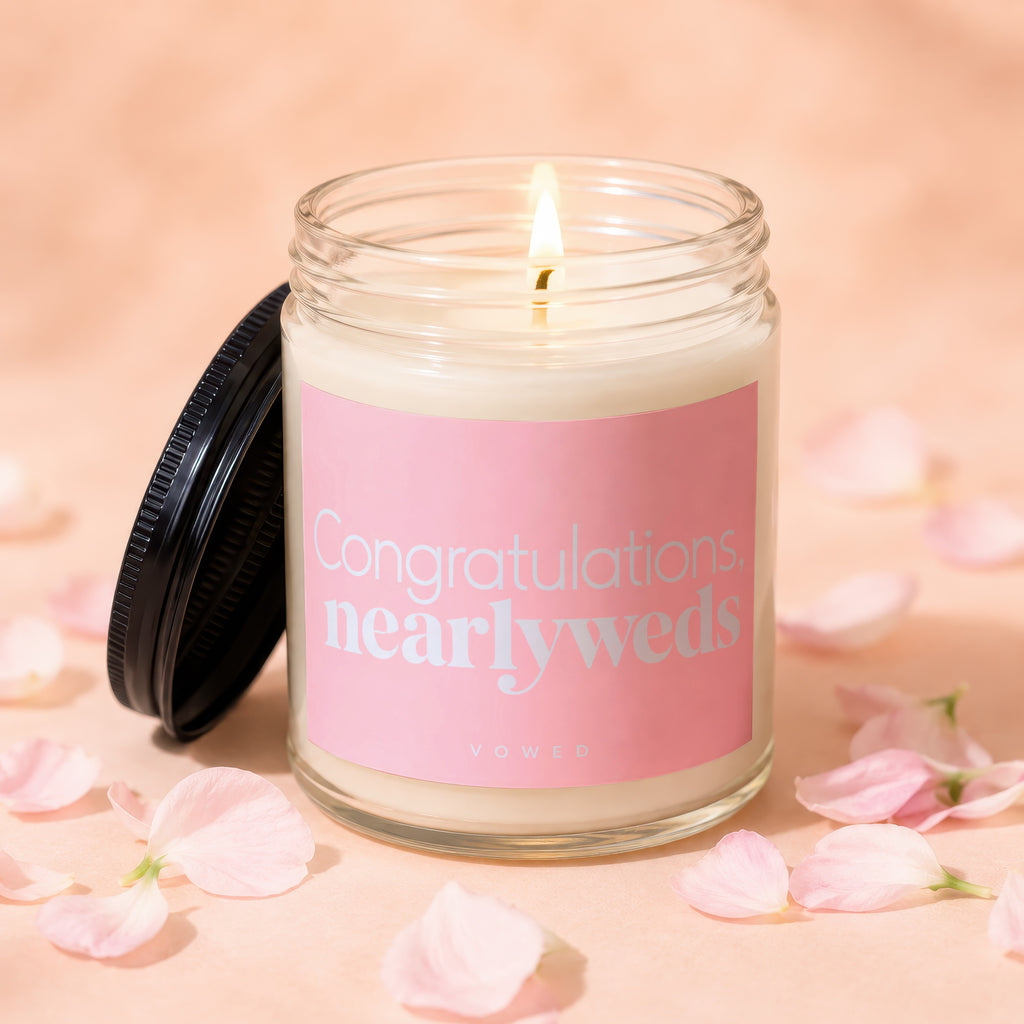 Congratulations, nearlyweds candle with lit wick on a peach background with pink petals.