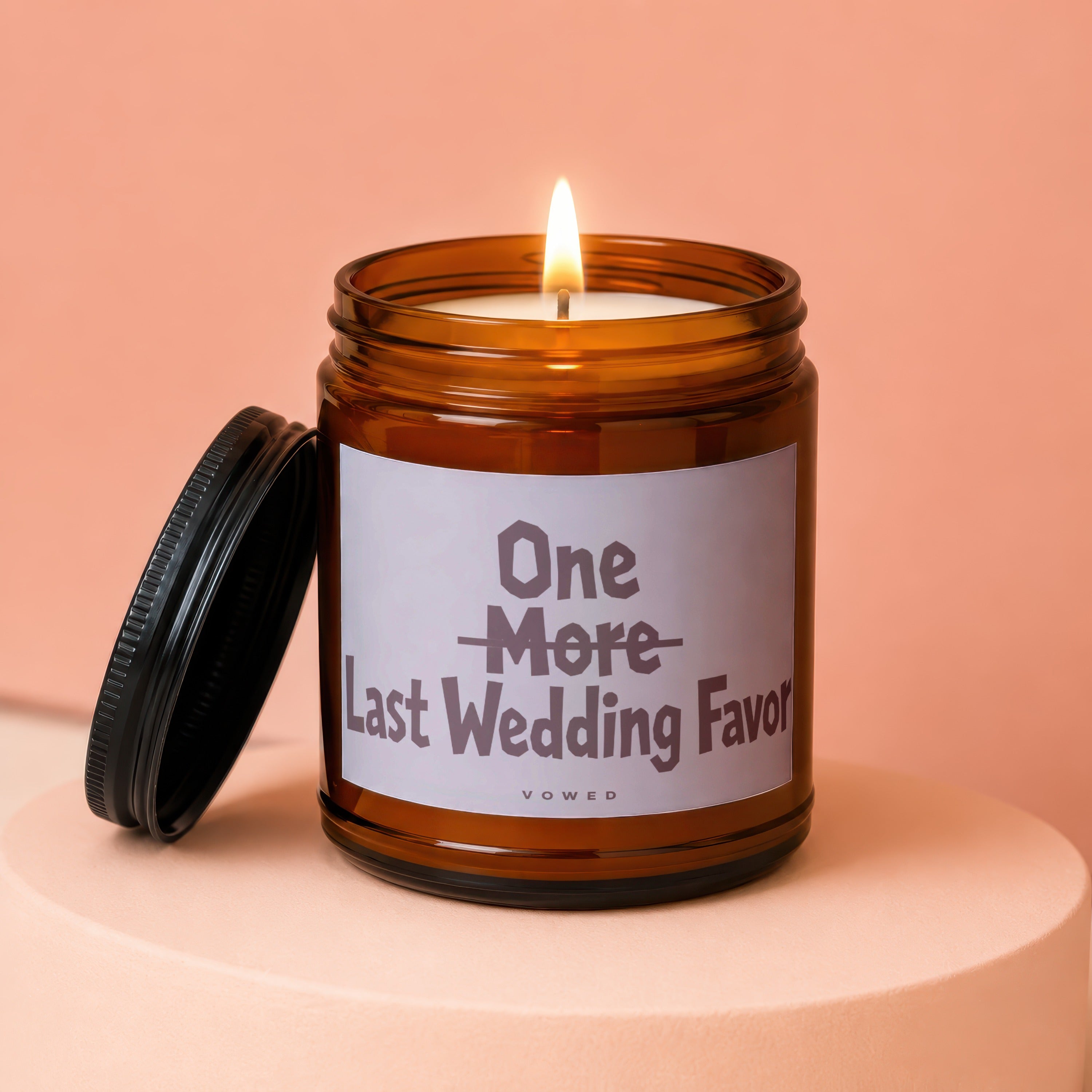 Amber jar candle with lit wick, lid off, labeled "One More Last Wedding Favor".