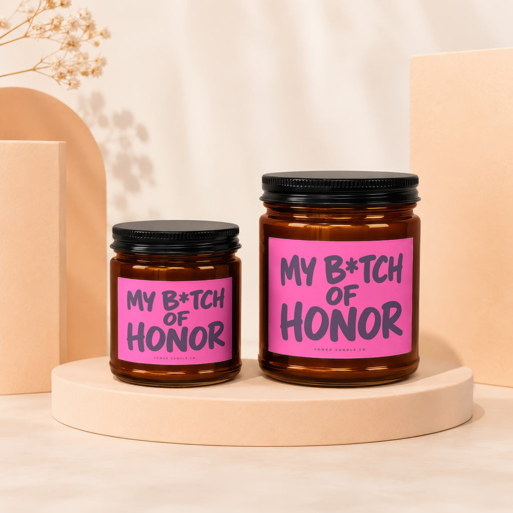 Two amber glass candles with pink labels reading "My B*tch of Honor".