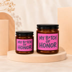 Two amber glass candles with pink labels reading "My B*tch of Honor".