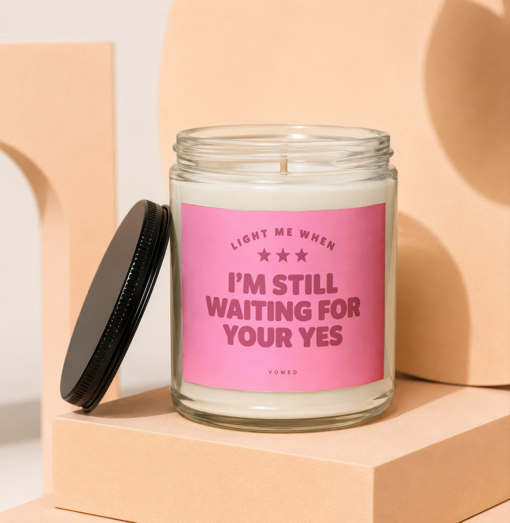 Glass candle with pink label reading "Light me when I'm still waiting for your yes".