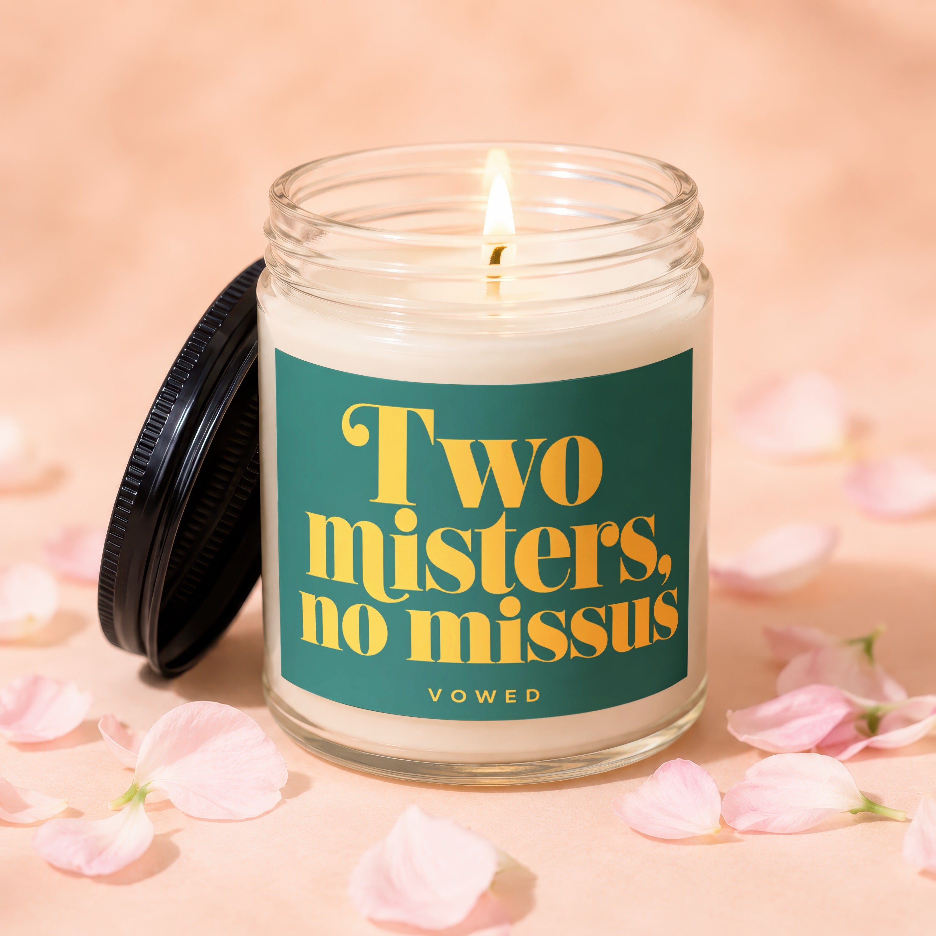 Candle with lit wick and lid off, displaying "Two misters, no missus" text.