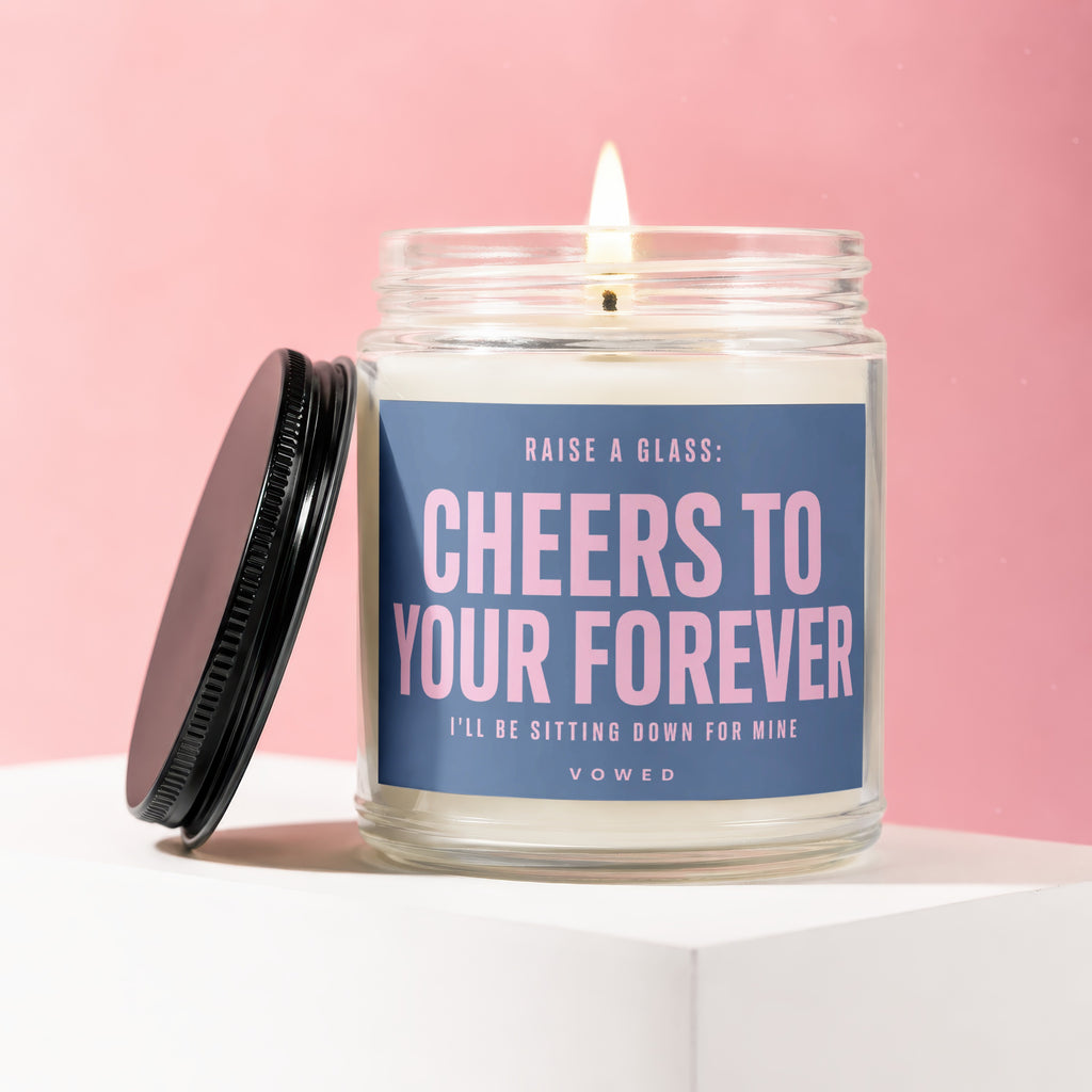 Lit candle with blue label reading "Cheers to Your Forever" and "Vowed".