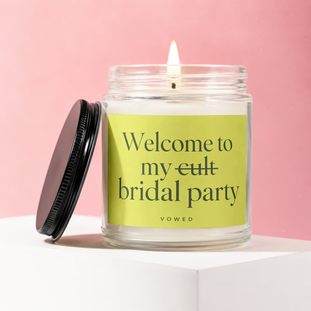 Lit candle in glass jar with black lid and "Welcome to my cult bridal party" label.