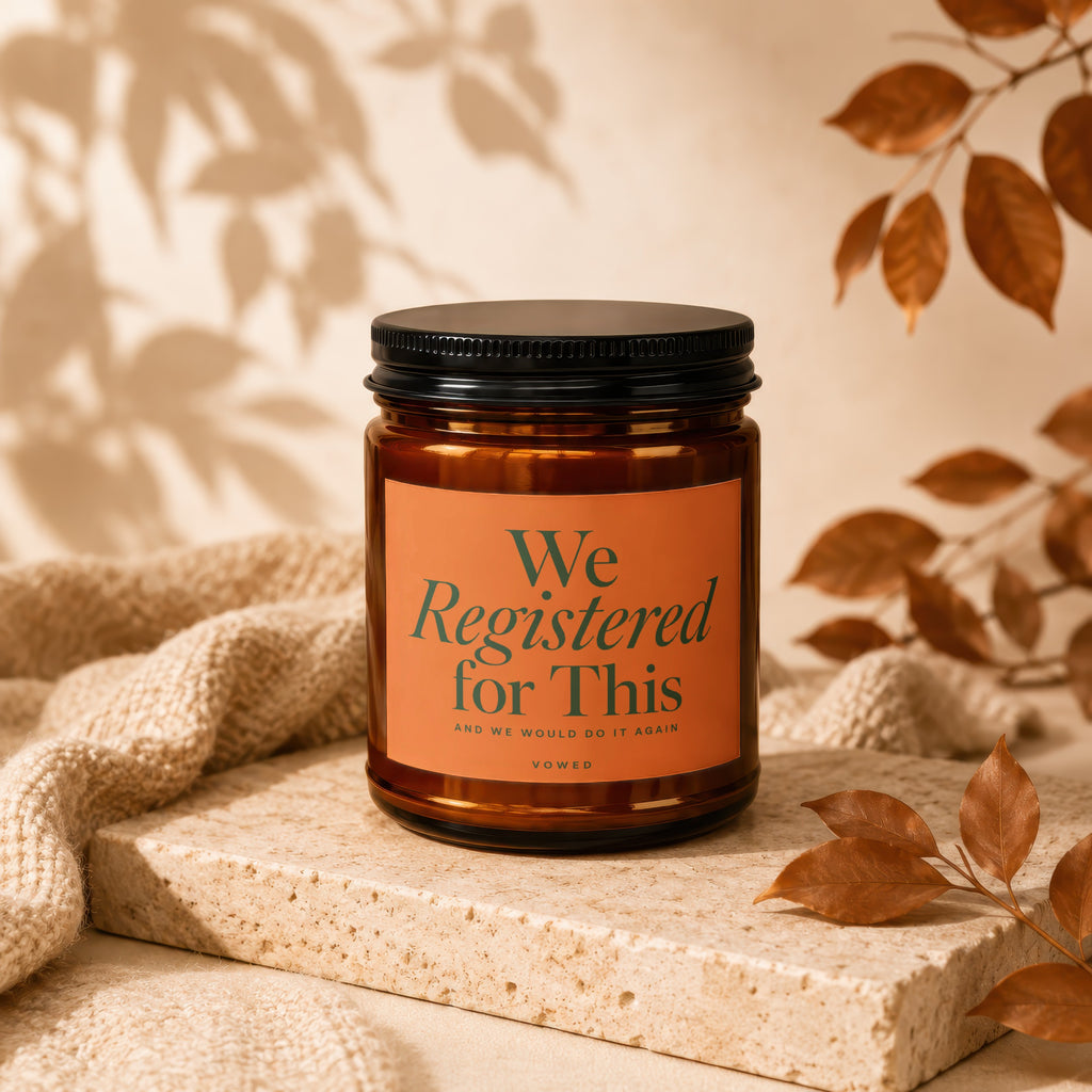 Amber candle with black lid and orange label reading "We Registered for This."
