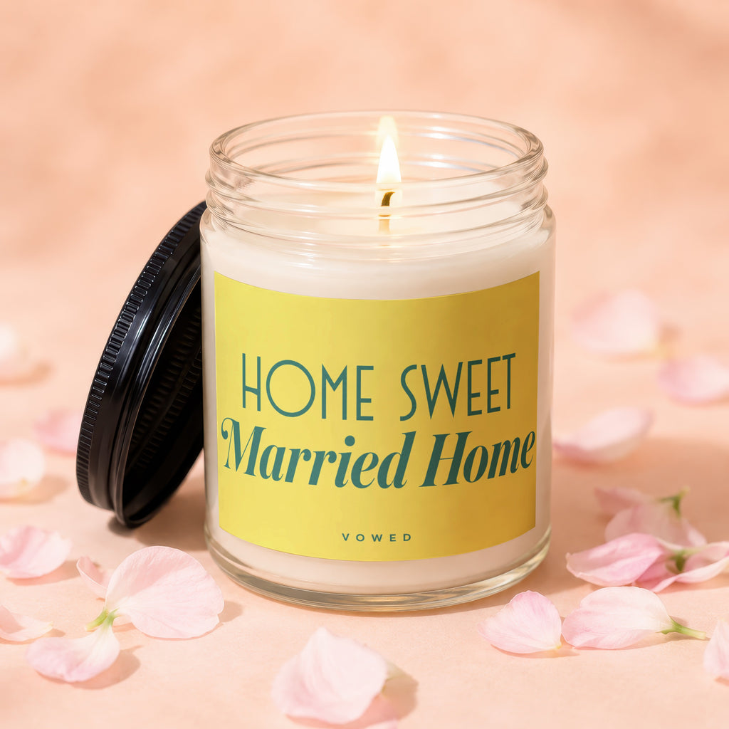 Glass jar candle with lit wick, yellow label reads "HOME SWEET Married Home VOWED".