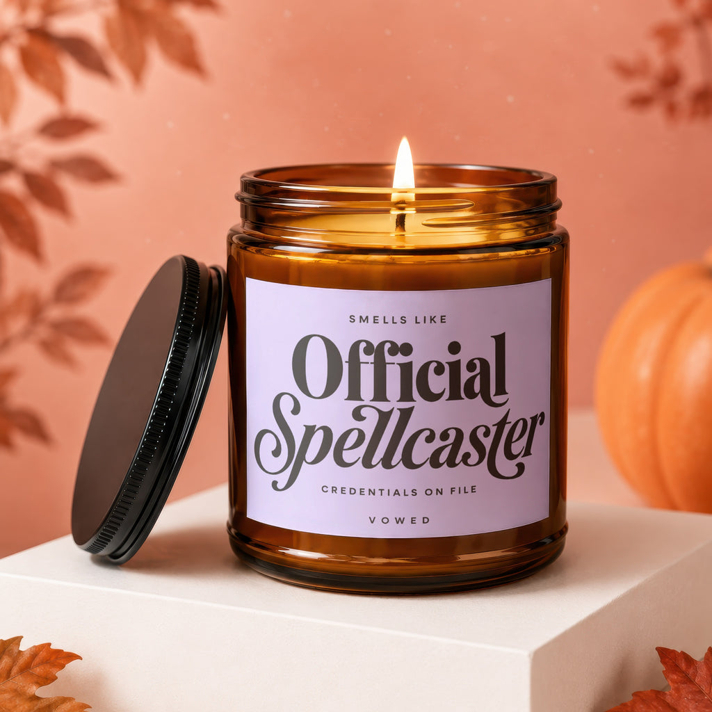 Brown glass candle with "Official Spellcaster" label, lit wick, and lid nearby.