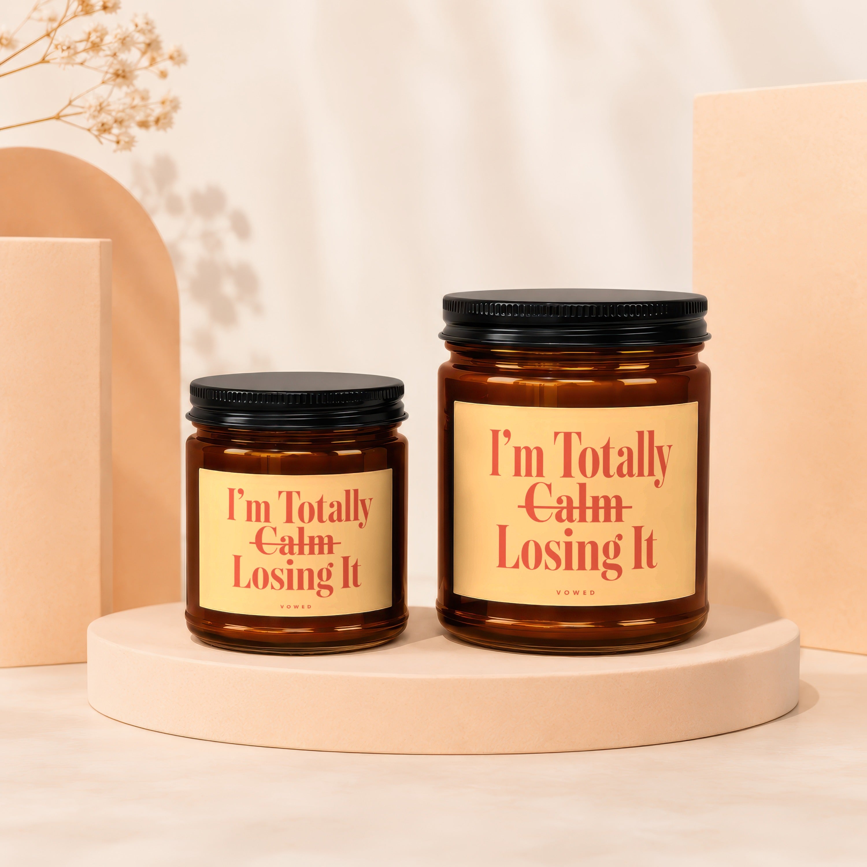 Two amber glass candles with black lids, featuring yellow labels that read "I'm Totally Calm Losing It."