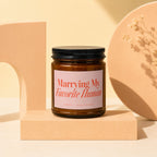 Amber candle with pink label reading "Marrying My Favorite Human" and "VOWED | HAND POURED".