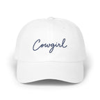 A white baseball cap with the word Cowgirl embroidered in blue cursive on the front panel.