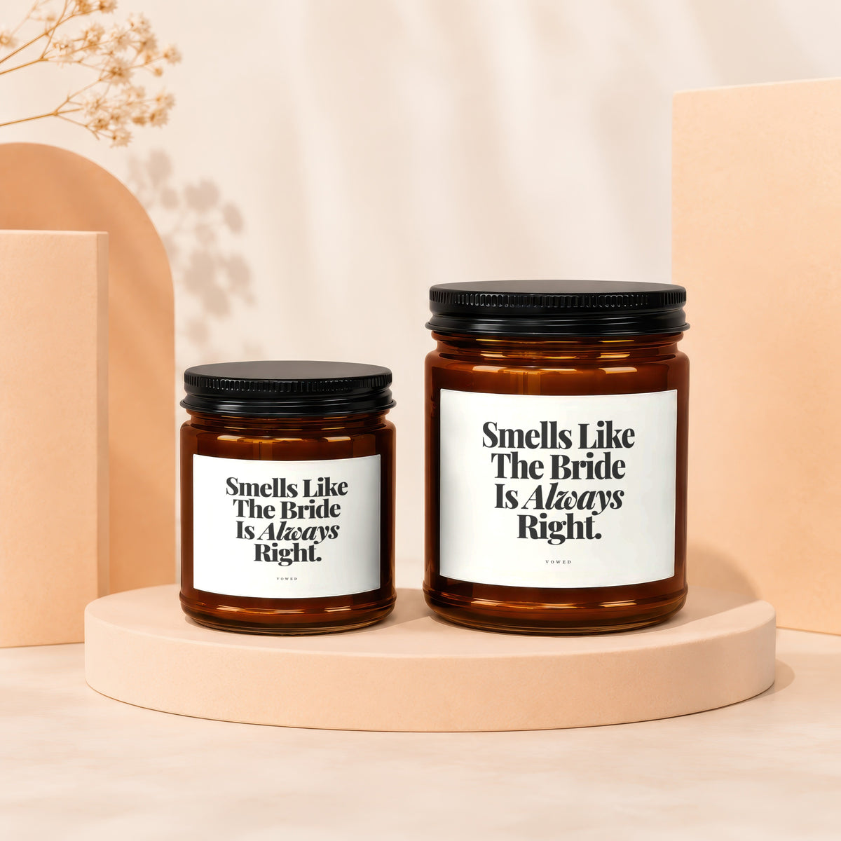 Two amber glass candles with black lids and white labels reading "Smells Like The Bride Is Always Right."