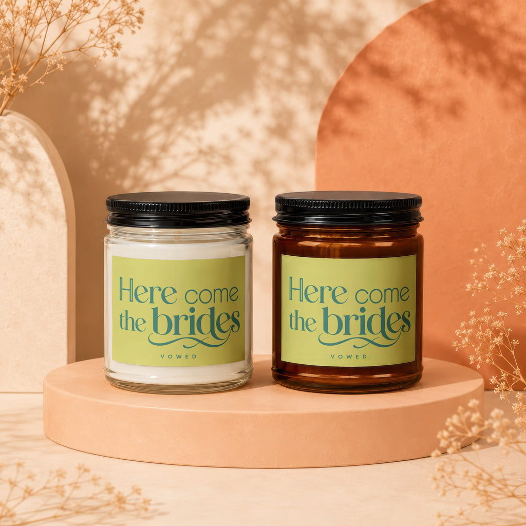 Two candles labeled "Here come the brides" from VOWED, one clear and one amber jar.