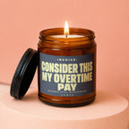 Amber jar candle with lit wick and black lid, reads "Invoice: Consider This My Overtime Pay".