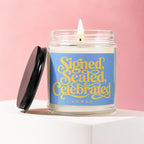 Lit candle in glass jar with blue label reading "Signed, Sealed, Celebrated VOWED".