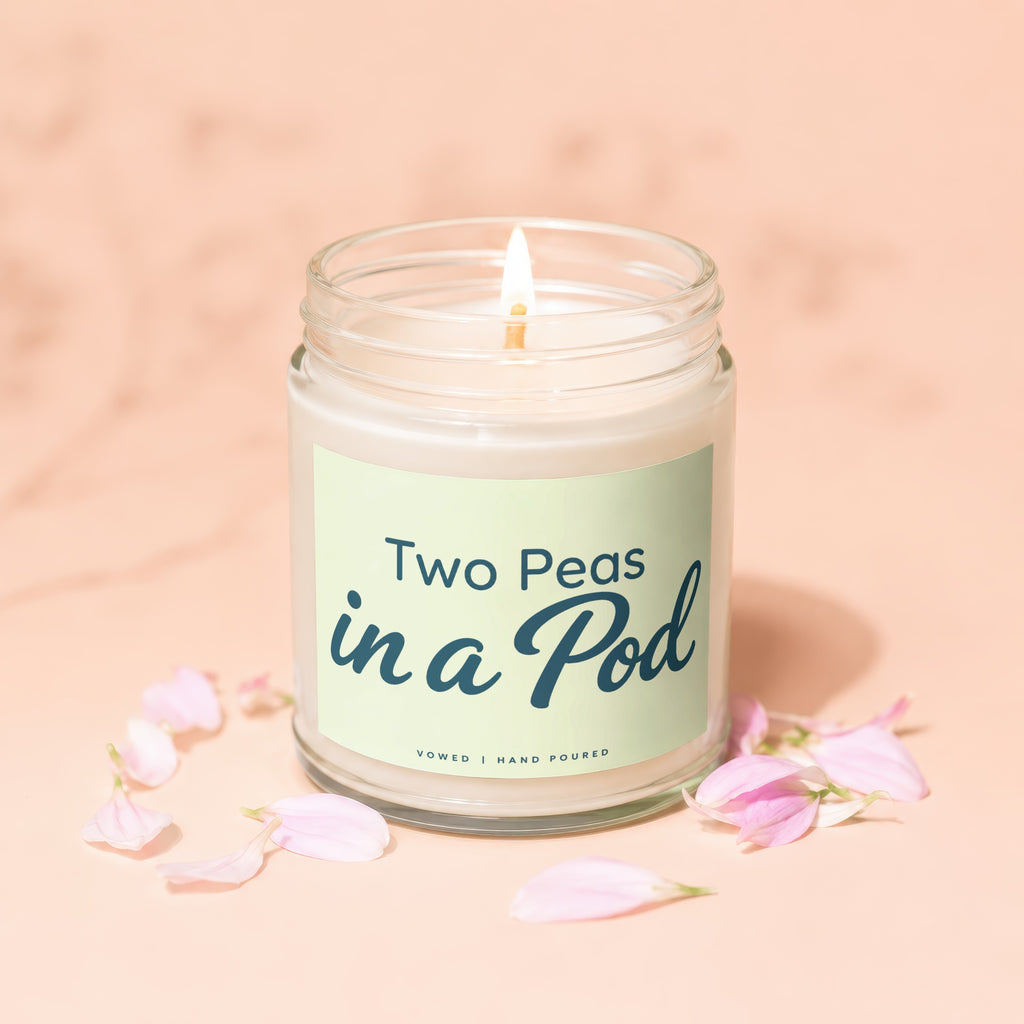 Candle labeled "Two Peas in a Pod" with lit wick and pink petals.