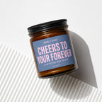 Amber jar candle with a blue label reading "Cheers to Your Forever" and "Vowed".
