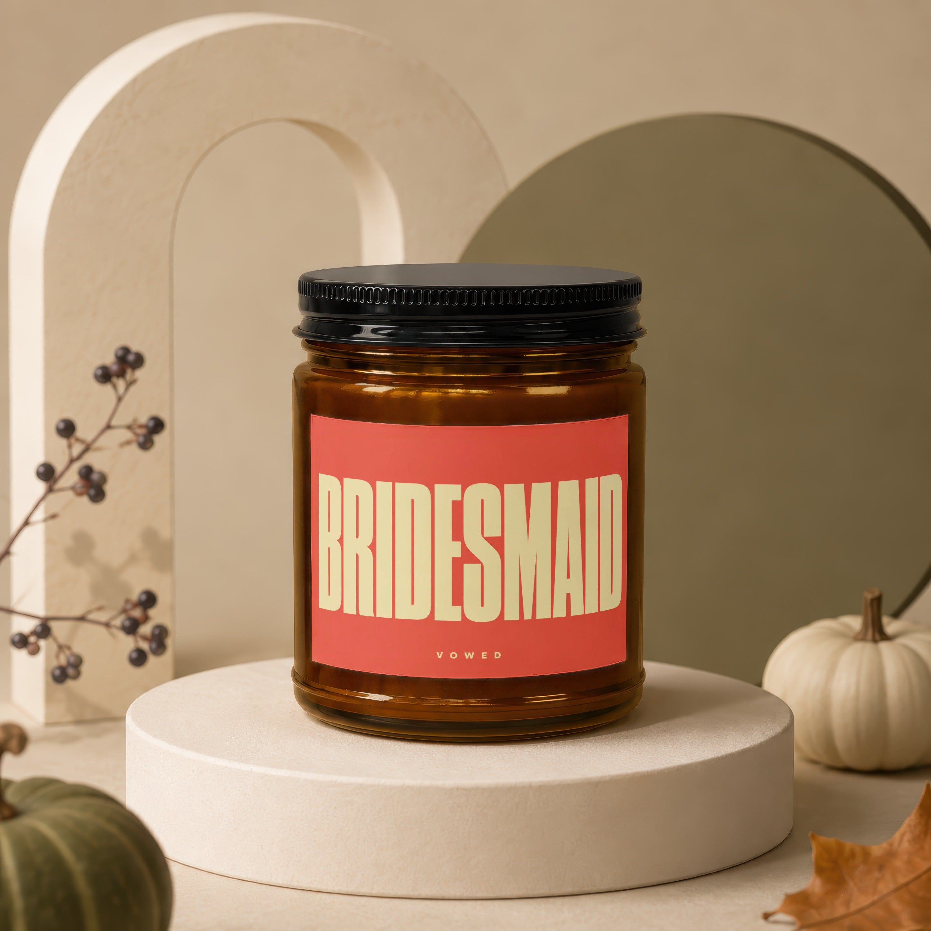 Amber candle with large "BRIDESMAID" text on a coral label, sits on a pedestal.