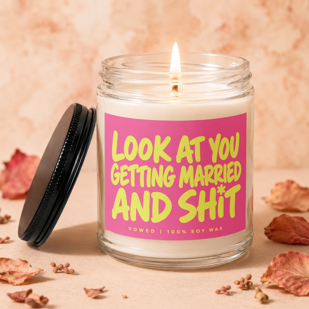 Glass jar candle with pink label reading "Look At You Getting Married and Shit".