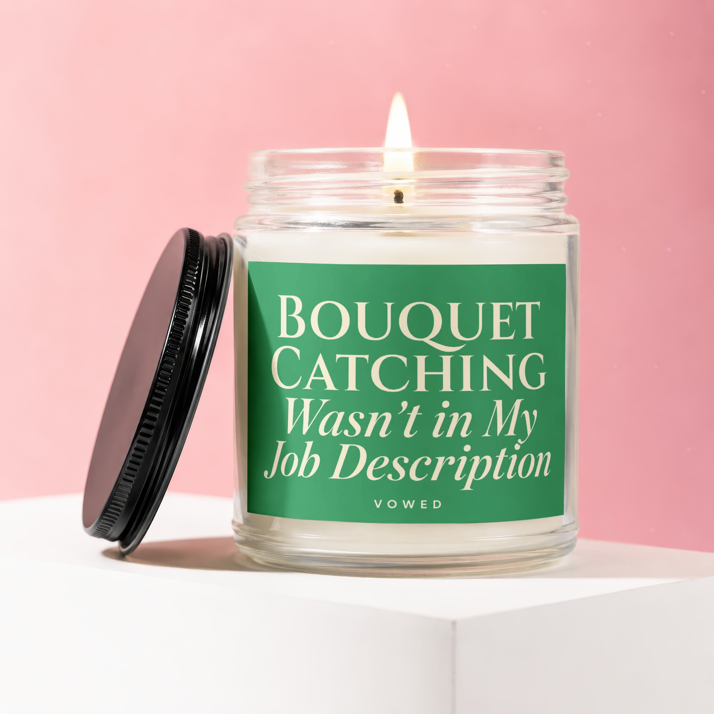Lit candle in glass with green label reading "BOUQUET CATCHING Wasn't in My Job Description."