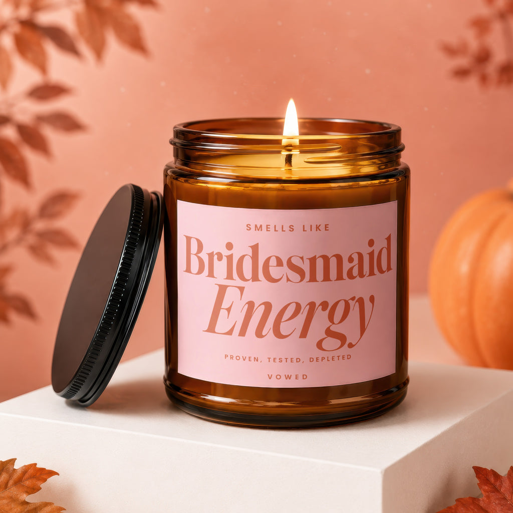 Amber glass candle with lit wick, pink label reads "Smells Like Bridesmaid Energy".