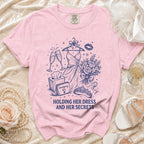 Pink t-shirt with "Holding Her Dress and Her Secrets" graphic and accessories.