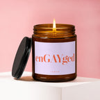 Lit amber glass candle with a white label that reads "enGAYged VOWED".