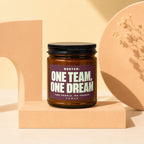 Amber jar candle with black lid, label reads "ROSTER: ONE TEAM, ONE DREAM TWO PEOPLE. NO TRADES. VOWED."