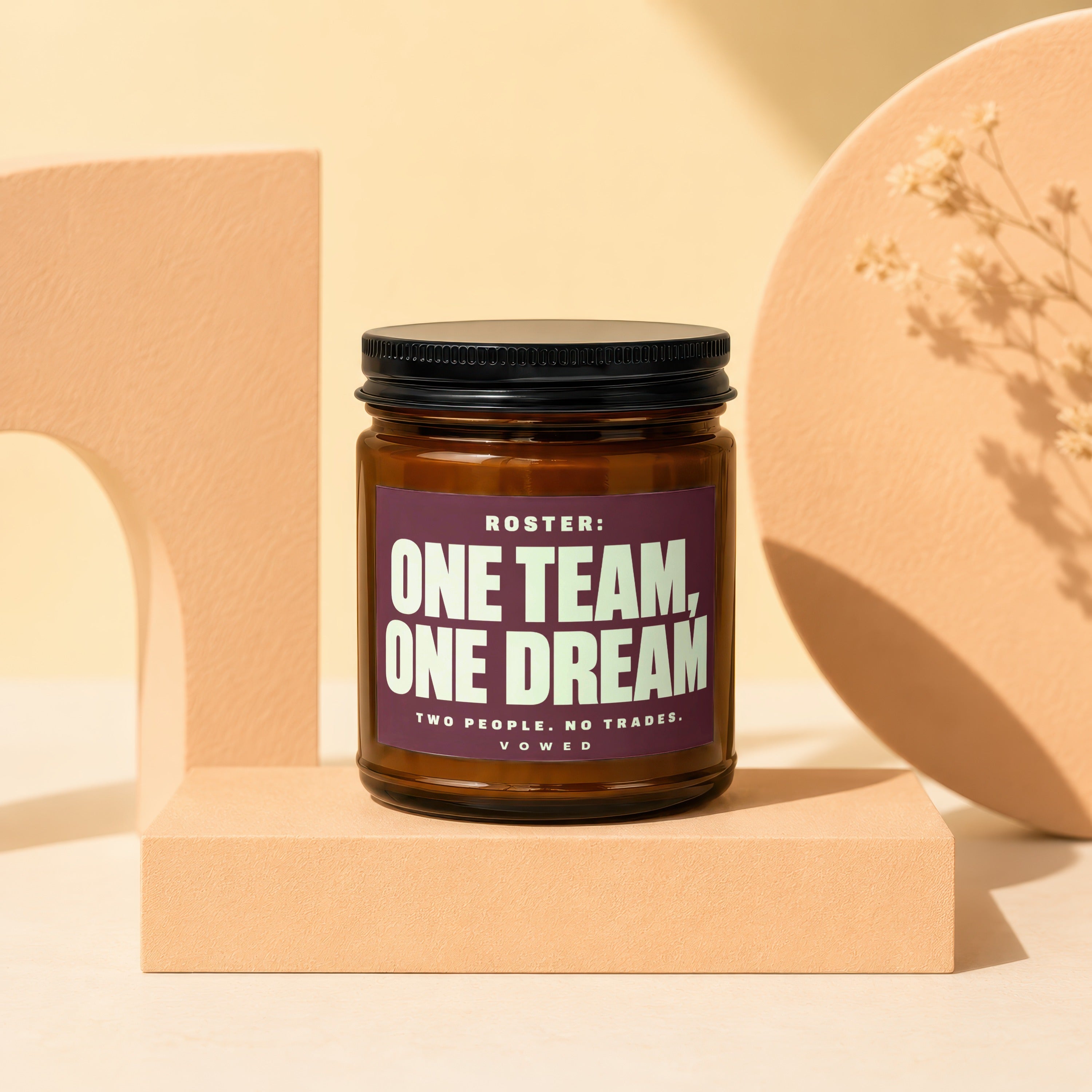Amber jar candle with black lid, label reads "ROSTER: ONE TEAM, ONE DREAM TWO PEOPLE. NO TRADES. VOWED."