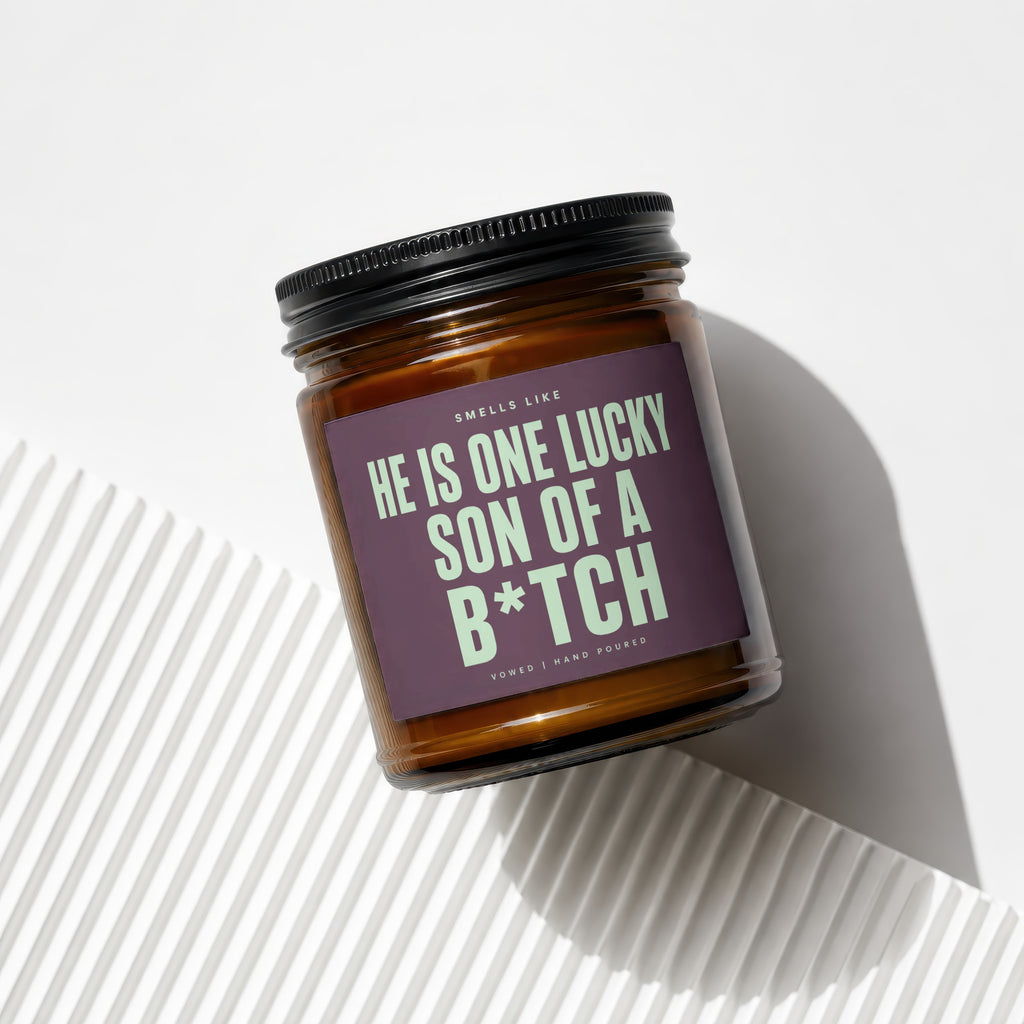 Brown glass candle with purple label that reads "Smells like he is one lucky son of a b*tch".