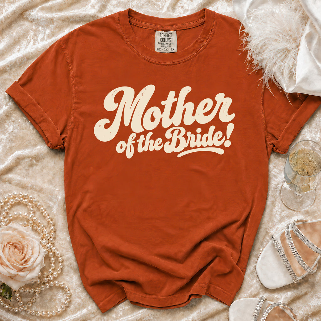 Orange t-shirt with "Mother of the Bride!" graphic, flat lay with accessories.