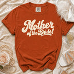 Orange t-shirt with "Mother of the Bride!" graphic, flat lay with accessories.