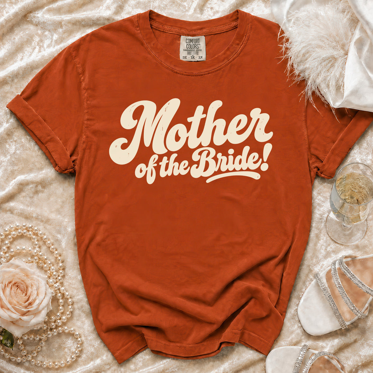 Orange t-shirt with "Mother of the Bride!" graphic, flat lay with accessories.