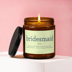 Amber glass candle with "bridesmaid noun professional dress fluffer..." text.
