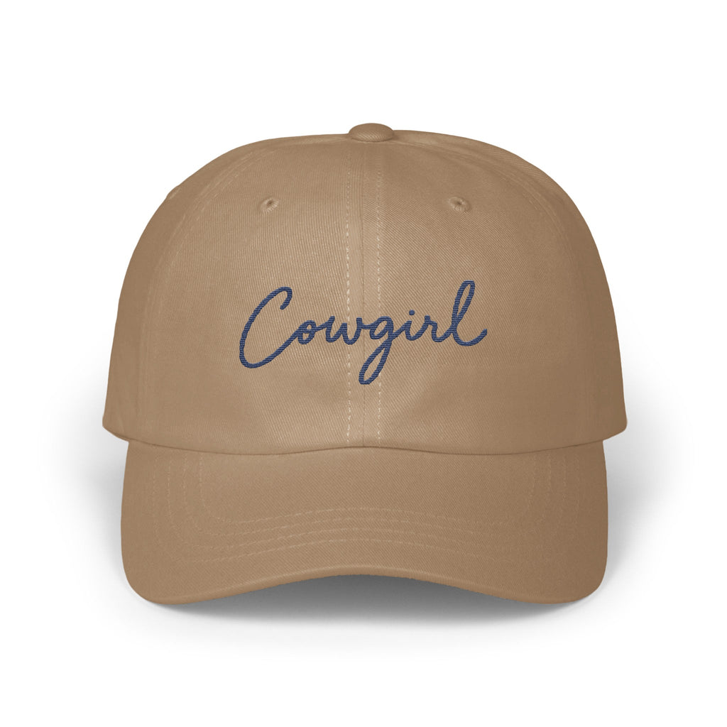 A tan baseball cap with the word Cowgirl embroidered in blue cursive on the front.
