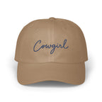 A tan baseball cap with the word Cowgirl embroidered in blue cursive on the front.