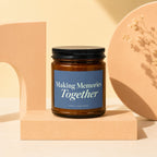 Amber glass candle with blue label reading "Making Memories Together" on pedestal.