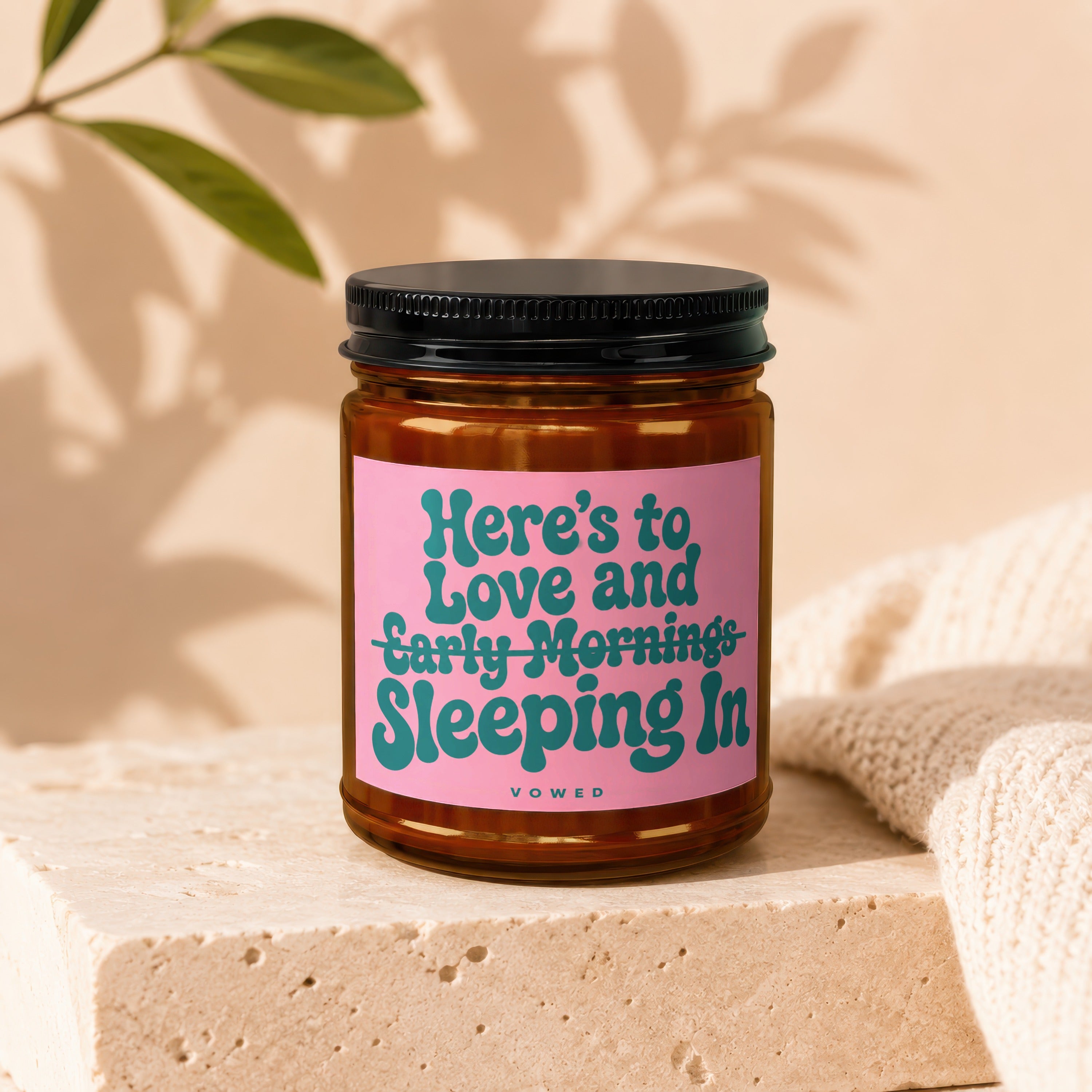 Amber jar candle with pink label reading "Here's to Love and Early Mornings Sleeping In".