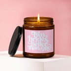 Lit candle in amber jar with black lid, pink label reads "Two brides, better than one."